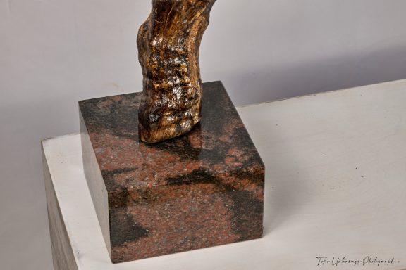Skulptur mit einer Füße-Detailaufnahme auf einem quadratischen Granitsockel.