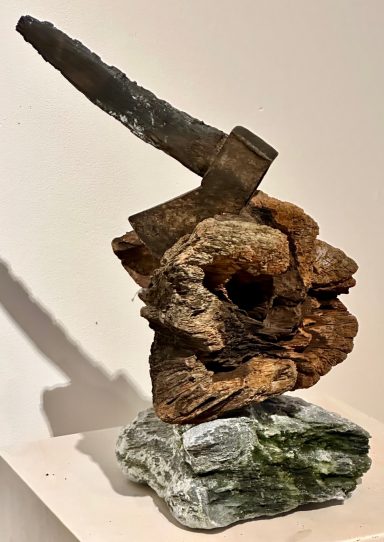 Moderne Skulptur aus Holz und Stein, mit einem Axtgriff oben.